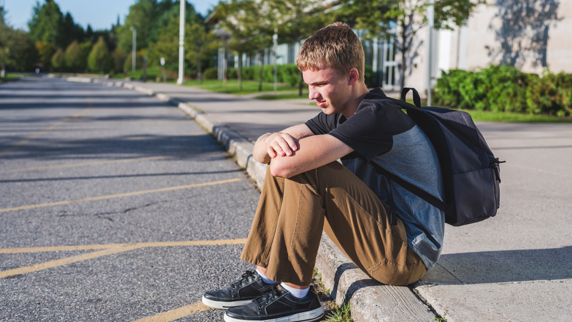 Einsamer Teenager sitzt am Straßenrand mit Schulrucksack