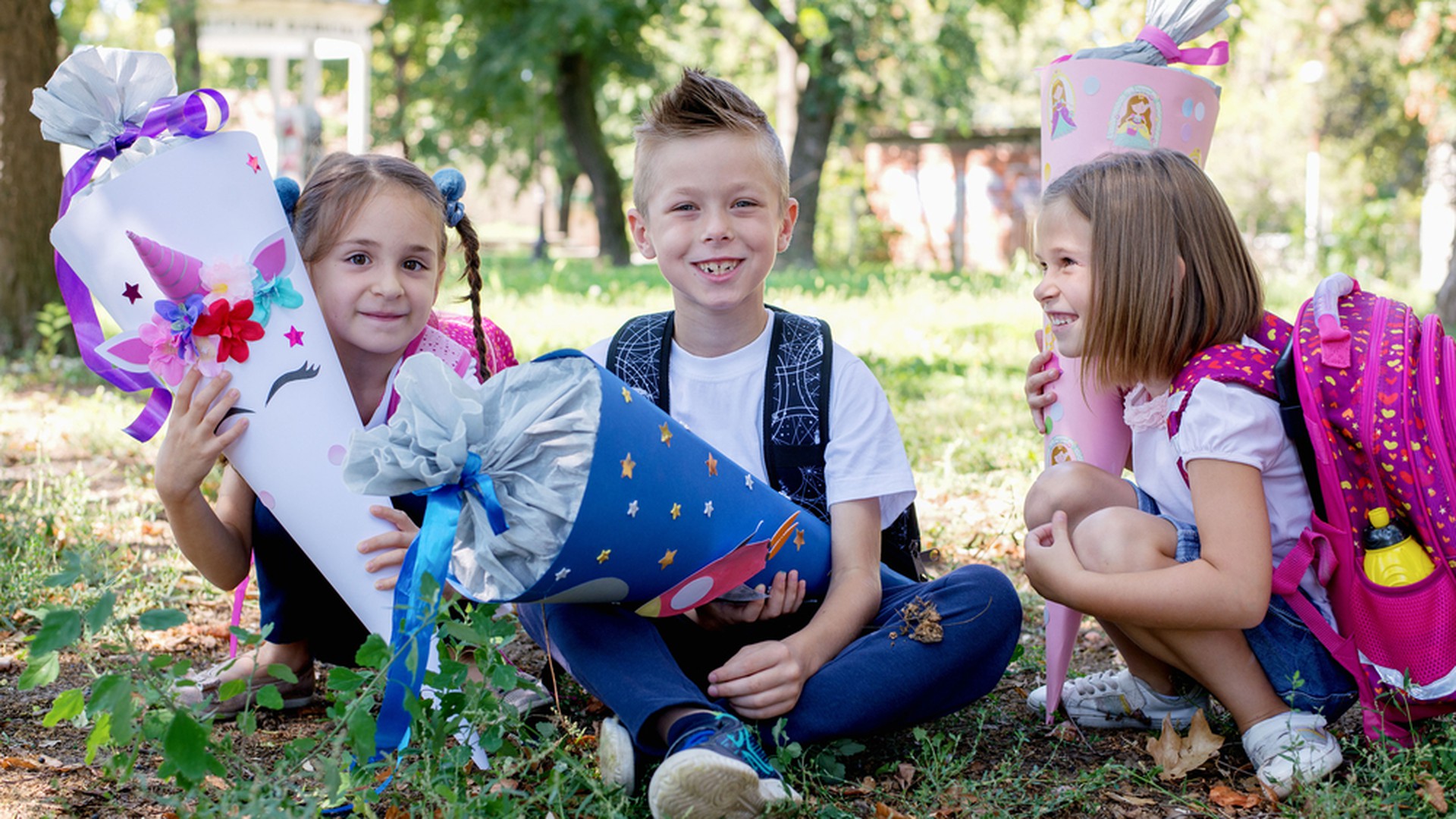 Kinder sitzen am ersten Schultag in der Wiese mit Schultüten